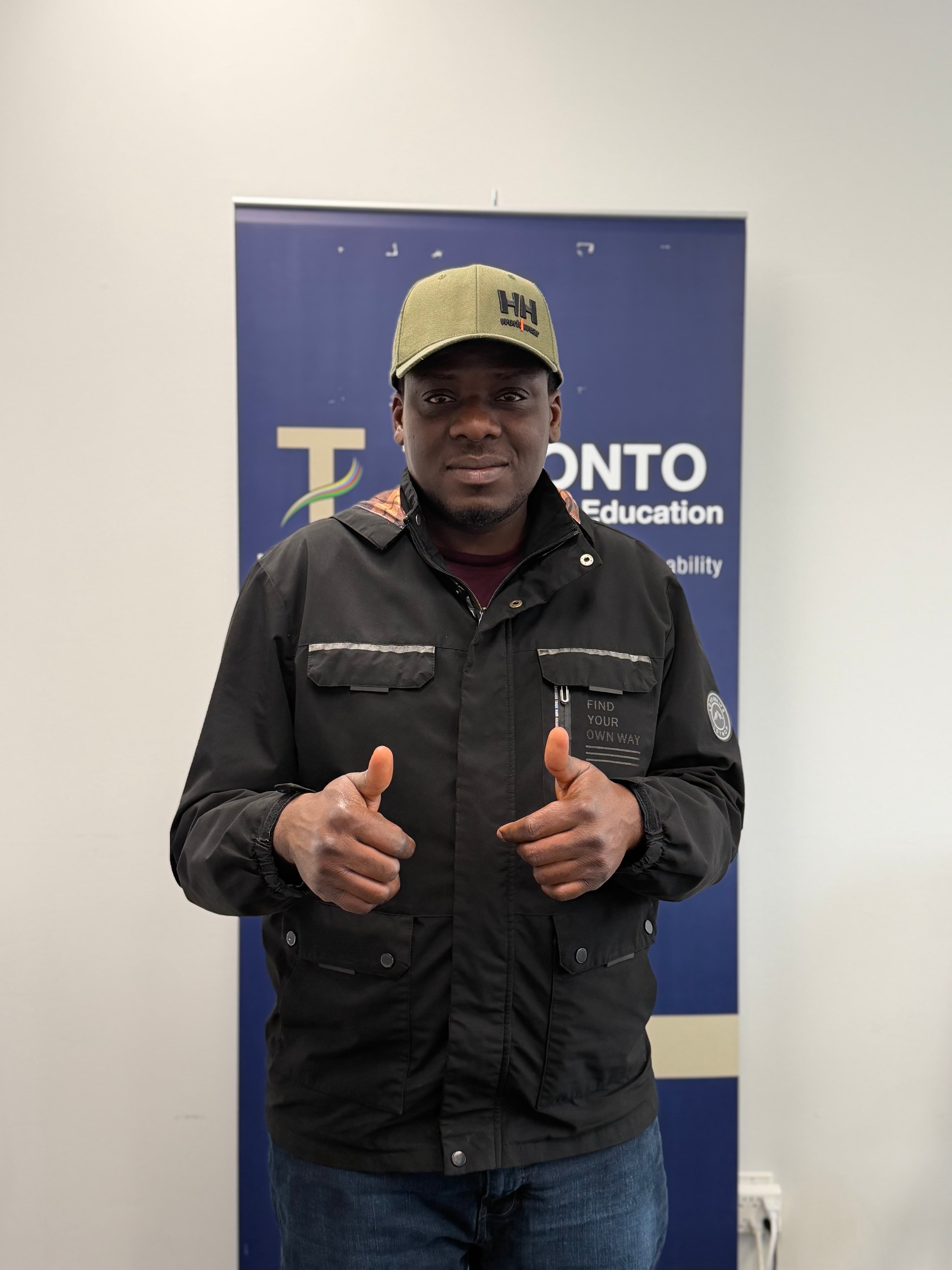 A student giving a thumbs up beside a Toronto Academy of Education banner
